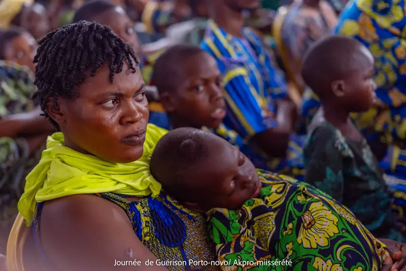 Une maman, son enfant endormi contre elle, attentive pendant la Journée de Guérison et de Solidarité à Akpro-Missérété